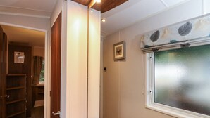 A room with a wooden bench, a window with a leaf pattern, and a door leading to another room. - Loch Lomond Holiday Home (Arrochar)
