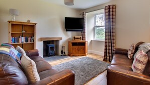 A living room with a fireplace, leather sofas, a bookshelf, and a TV mounted on the wall. - 4 Bed in Gayle (oc-ds950) (Hawes)