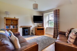 Una sala de estar con chimenea, sofás de cuero, una estantería y un televisor montado en la pared.