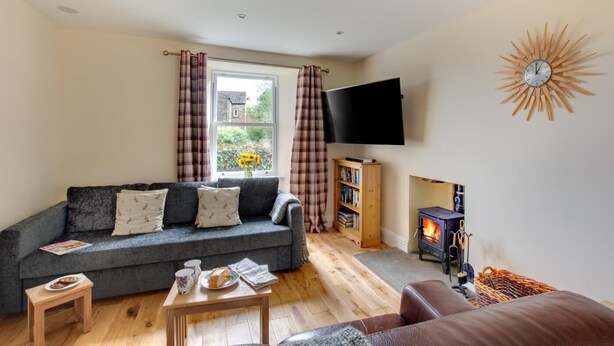 A living room with a sofa, a small table with items, a fireplace, a bookshelf, and a TV mounted on the wall. - 4 Bed in Gayle (oc-ds950) (Hawes)