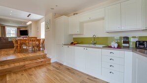 A modern kitchen with white cabinets, a wooden dining table, and a staircase leading to another room. - 4 Bed in Gayle (oc-ds950) (Hawes)