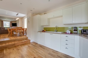 Une cuisine moderne avec des meubles blancs, une table à manger en bois et un escalier menant à une autre pièce.