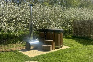 Ein tragbarer Grill für den Außenbereich mit Schornstein, einem Whirlpool und einer Holzterrasse in einem Garten.