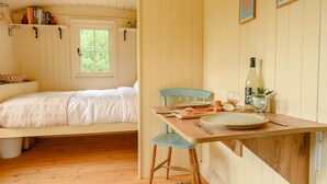 Ein gemütliches Zimmer mit einem Bett, einem Esstisch mit Stühlen, einem Fenster und einem Regal mit Büchern und Dekoration.