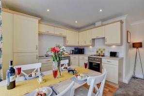 A modern kitchen with white cabinets, a dining table set with plates, glasses, and a vase of flowers. - 2 Bed in Whitby (oc-w463) (Whitby)
