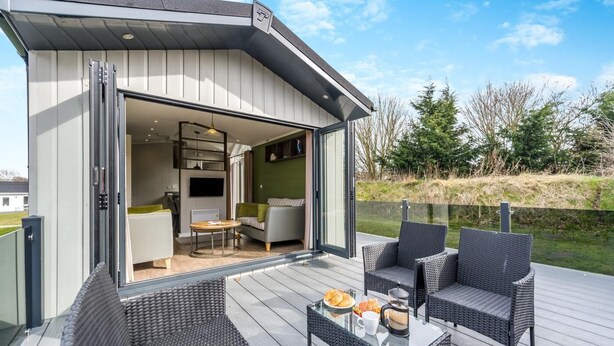 Um espaço de estar moderno ao ar livre, com porta de vidro que dá para um interior mobiliado, móveis de vime e uma vista desobstruída da paisagem circundante.