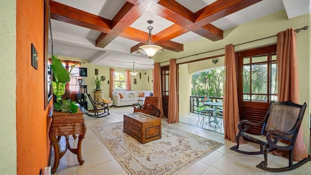 A spacious living room with a large wooden ceiling, a rocking chair, a sofa, and a dining area with a table and chairs. - Serenity Villa - by Zenbreak (Speightstown)