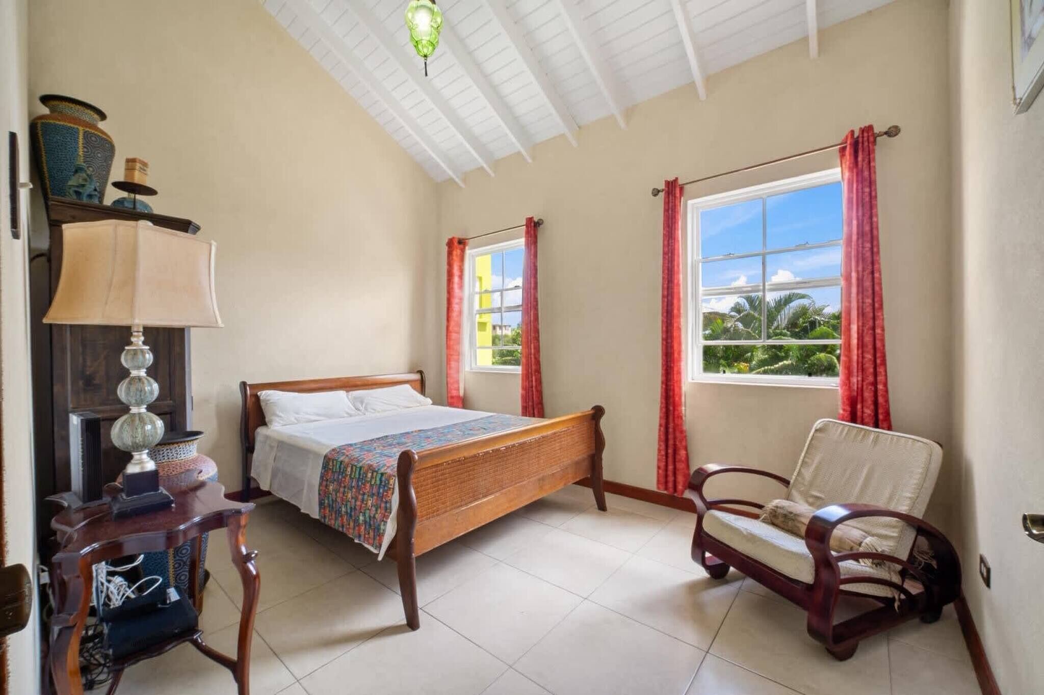 Un dormitorio con cama de madera, una silla, un escritorio con lámpara y una ventana con cortinas.