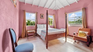A bedroom with a four-poster bed, a chair, a small table, and a window with curtains. - Serenity Villa - by Zenbreak (Speightstown)
