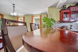 Un comedor con mesa de madera, sillas, una planta grande y una cocina con armarios rojos.