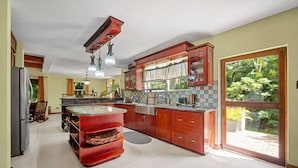 A spacious kitchen with a large island, wooden cabinets, and a sliding glass door to the outdoors. - Serenity Villa - by Zenbreak (Speightstown)