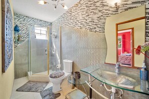 Un baño moderno con cabina de ducha de vidrio, lavamanos de vidrio y un inodoro a la vista.