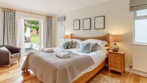 Une chambre à coucher avec un lit, des lampes de chevet, une table de chevet en bois, une chaise et une vue sur l’extérieur.