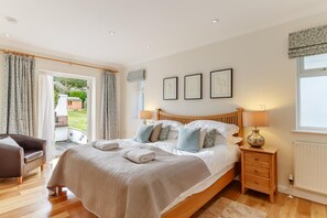Ein Schlafzimmer mit einem Bett, Nachttischlampen, einem Holznachttisch, einem Sessel und Blick ins Freie.