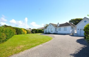 A two-story house with a driveway leading to a garage, surrounded by well-maintained lawns and hedges. - 6 Bed in Padstow (oc-p00774) (Constantine Bay)
