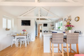 A spacious kitchen with a central island, white cabinetry, and a dining area with wicker chairs. - 2 Bed in Holt (oc-2027) (Thornage)