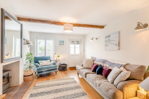 Een gezellige woonkamer met een open haard, een blauwe fauteuil, een beige bank en een grote spiegel.