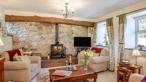 Una sala de estar acogedora con pared de piedra, chimenea, televisión y asientos cómodos.