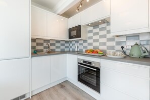 Eine moderne Küche mit weißen Schränken, einer Mikrowelle, einem Backofen und einer karierten Spritzschutzwand.