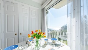 Une table à manger dressée avec des assiettes blanches, des bols bleus et des verres transparents, et un vase de tulipes posé sur la table.