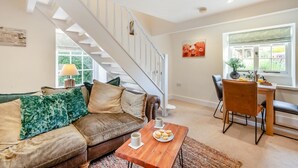 A modern living room with a staircase, a dining area, and a view of greenery outside. - 2 Bed in Heacham (oc-2013) (Heacham)