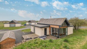 A modern house with a large glass front, a wooden deck, and a paved driveway. - 3 Bed in Bamburgh (oc-w31886) (Bamburgh)