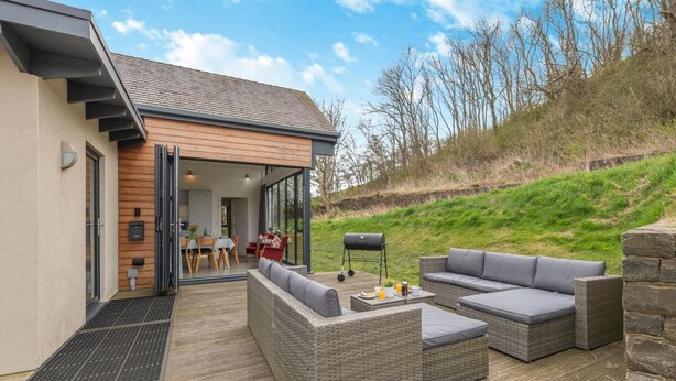 A modern house with a patio area featuring wicker furniture and a barbecue grill. - 3 Bed in Bamburgh (oc-w31886) (Bamburgh)