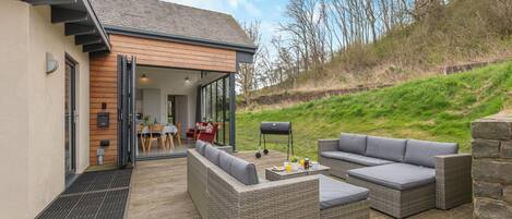 A modern house with a patio area featuring wicker furniture and a barbecue grill.