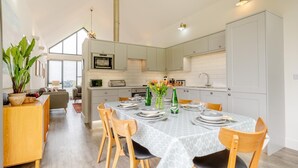 A modern kitchen with a dining area, featuring a large table set for four, a microwave, and a toaster. - 3 Bed in Bamburgh (oc-w31886) (Bamburgh)