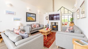 A modern living room with a fireplace, grey sofas, a flat-screen TV, and artwork on the walls. - 3 Bed in Bamburgh (oc-w31886) (Bamburgh)
