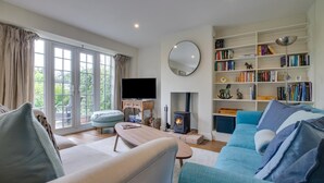 A living room with a sofa, a television, a bookshelf, and a fireplace. - 4 Bed in Walberswick (oc-4ms) (Walberswick)