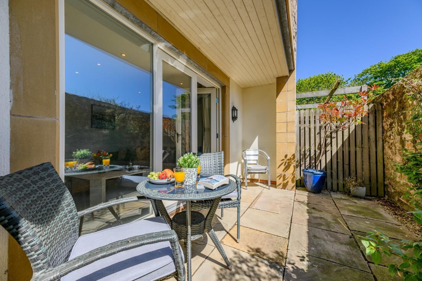 A patio with wicker furniture, a table with a plate of fruit, and a blue pot.