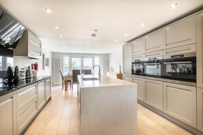 A modern kitchen with a marble island, stainless steel appliances, and a dining area with a view. - 3 Bed in Beadnell (oc-gd1567) (Beadnell)