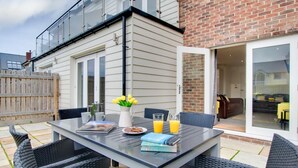 An outdoor patio with a table set for two, a chair, a small garden, and a brick wall. - 4 Bed in Beadnell (oc-gd1280) (Beadnell)