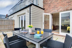 An outdoor patio with a table set for two, a chair, a small garden, and a brick wall. - 4 Bed in Beadnell (oc-gd1280) (Beadnell)
