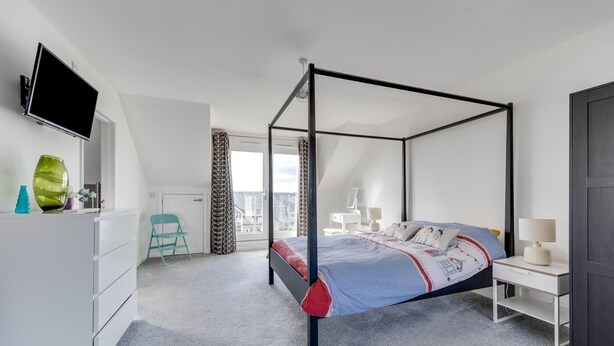 A modern bedroom with a four-poster bed, a flat-screen TV mounted on the wall, a desk with a chair, and a window with curtains. - 4 Bed in Beadnell (oc-gd1280) (Beadnell)