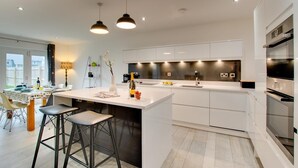 A modern kitchen with a central island, bar stools, pendant lighting, and a view of the outdoors. - 4 Bed in Beadnell (oc-gd1280) (Beadnell)