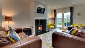 A living room with leather sofas, a fireplace, a flat-screen TV, and a sliding glass door leading to an outdoor area. - 4 Bed in Beadnell (oc-gd1280) (Beadnell)