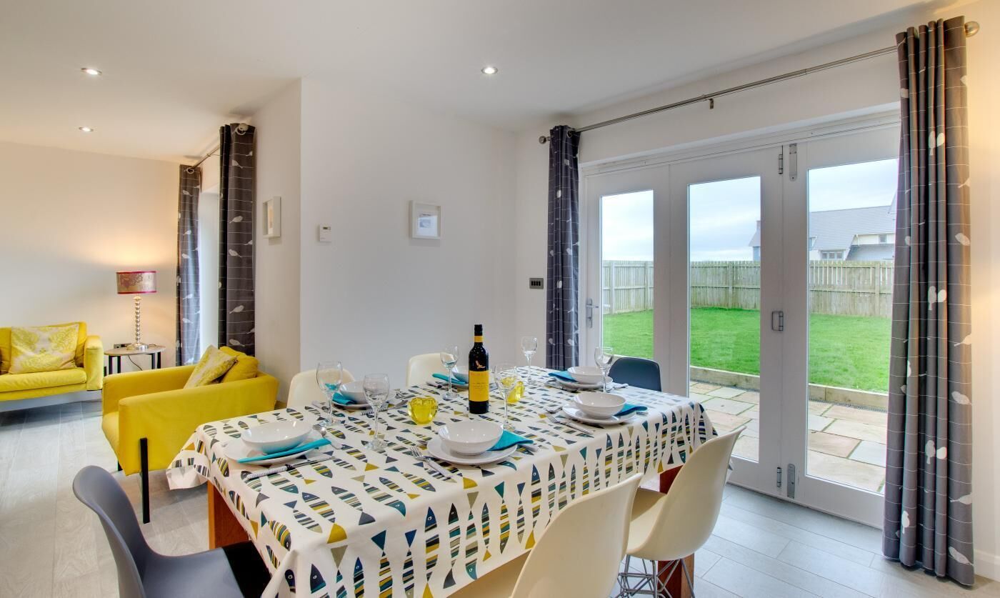 A dining area with a table set for four, a yellow sofa, and a view of a grassy yard through glass doors.