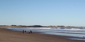 A beach with a wide sandy shore, gentle waves, and a clear sky. - 4 Bed in Beadnell (oc-gd1280) (Beadnell)