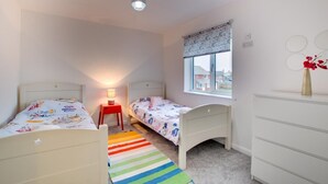 A bedroom with two single beds, a nightstand with a lamp, a window with a view, and a dresser. - 4 Bed in Beadnell (oc-gd1280) (Beadnell)
