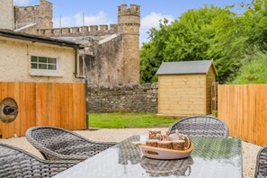 A patio with wicker chairs and a table, a wooden fence, and a stone wall with a tower in the background. - 2 Bed in Brough (oc-c31900) (Church Brough)