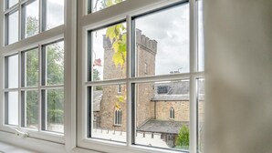 Blick durch ein Fenster mit mehreren Scheiben auf ein Steingebäude mit einem Turm und Rundbogenfenstern.