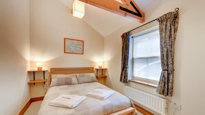A bedroom with a wooden bed, bedside lamps, a window with curtains, and a radiator. - 2 Bed in Seahouses (oc-gd1314) (Seahouses)