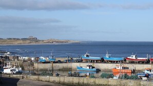 A coastal harbor with several boats docked, a sandy beach, and a distant hill. - 2 Bed in Seahouses (oc-gd1314) (Seahouses)