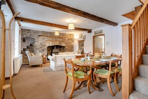 Un coin repas chaleureux avec une cheminée en pierre, des poutres en bois et un escalier.