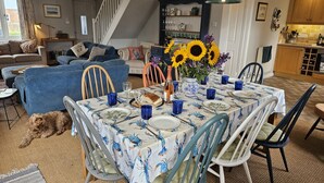 A dining area with a table set for four, surrounded by chairs. A dog is visible in the foreground. - 4 Bed in Beadnell (oc-gd1697) (Beadnell)