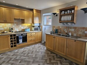 A kitchen with wooden cabinets, a herringbone-patterned floor, a built-in wine rack, a microwave, a kettle, and a dish rack on the wall. - 4 Bed in Beadnell (oc-gd1697) (Beadnell)