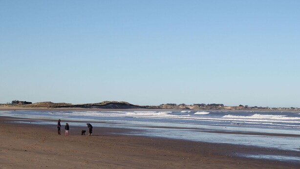 A wide sandy beach with gentle waves, a few people, and distant hills. - 4 Bed in Beadnell (oc-gd1697) (Beadnell)