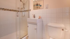 A bathroom with a glass-enclosed shower, a white sink with a mirror above it, and a toilet. - 4 Bed in Beadnell (oc-gd1697) (Beadnell)